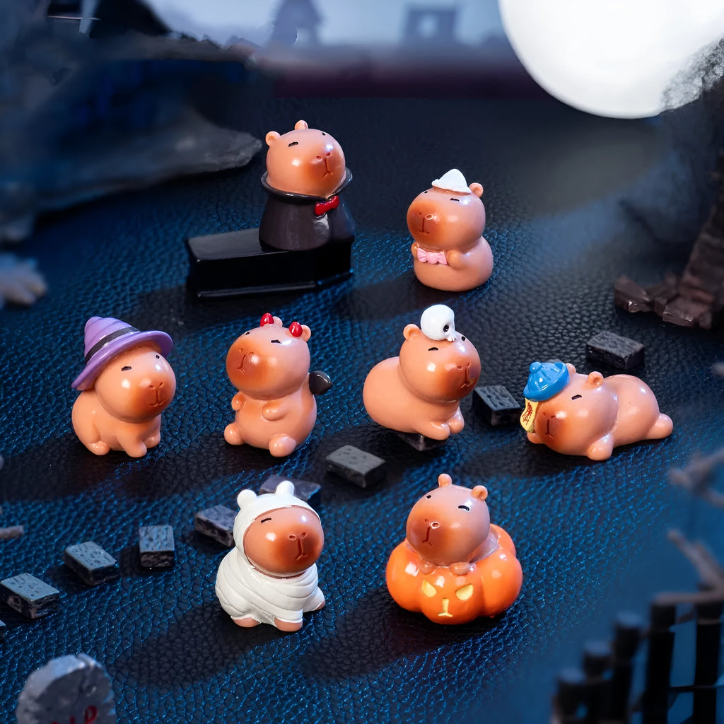 Set of eight small Halloween-themed capybara resin figurines on a wooden surface.