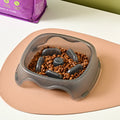 A blue plastic dog slow feeder bowl designed to prevent choking, shown alongside grey, green, and orange colour options.