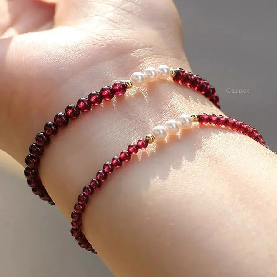 Close-up of a women's adjustable crystal bracelet with red garnet and white artificial pearl beads.