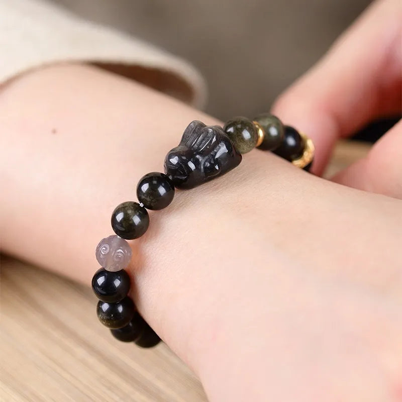 Handmade grey obsidian lying rabbit bracelet with brass and silver details on a wrist, shown in 8mm and 10mm size options.