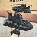 Men's black casual sneaker with thick rubber sole, mesh upper, abstract pattern, and lace-up front.