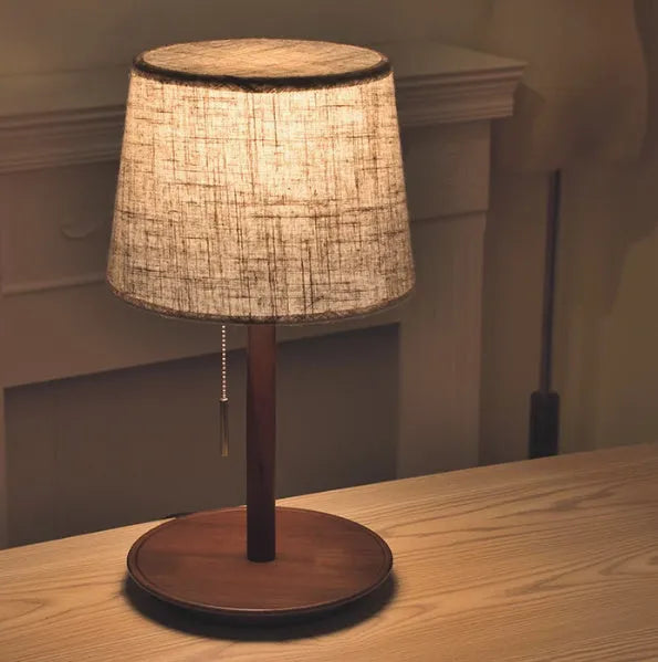 Walnut colour solid wood bedside lamp with a white fabric shade on a wooden surface.
