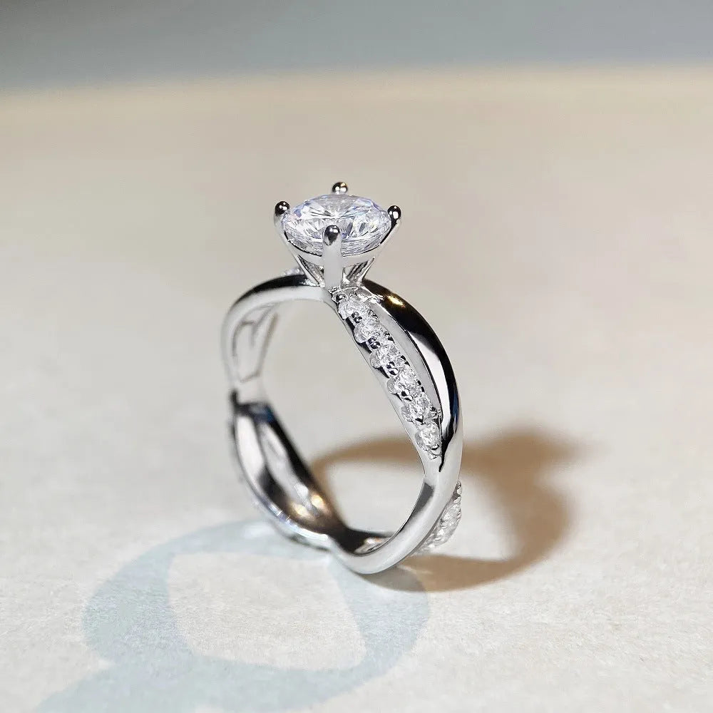 Geometric silver moissanite ring with twisted arm design and four-claw setting, shown in white diamond colour.
