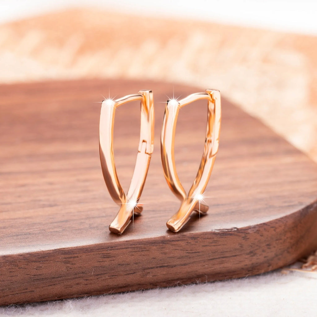Pair of rose gold cross-shaped earrings on a plain background, showing pierced post design.