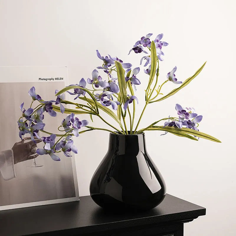Black ceramic round belly vase with coloured glaze finish and two white orchid flowers displayed on wooden surface