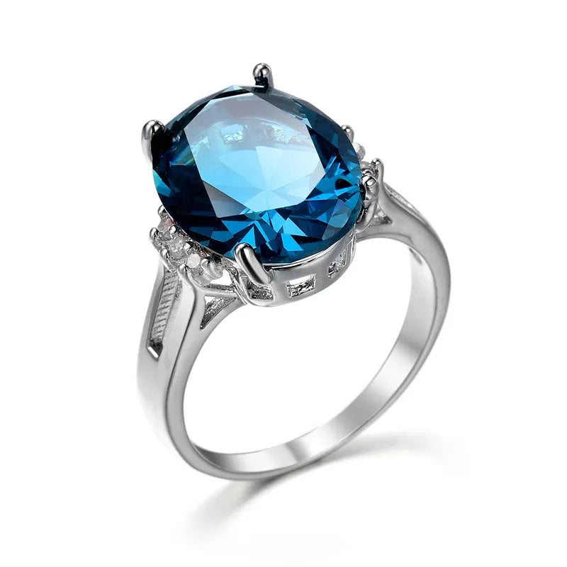 Geometric ellipse-shaped copper ring with zircon decoration in blue black finish on a grey background.
