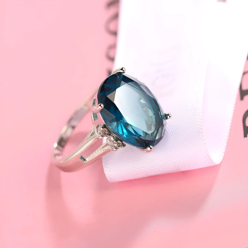 Geometric ellipse-shaped copper ring with zircon decoration in blue black finish on a grey background.