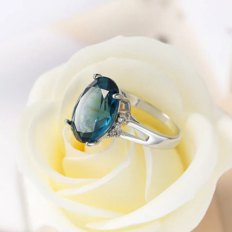 Geometric ellipse-shaped copper ring with zircon decoration in blue black finish on a grey background.