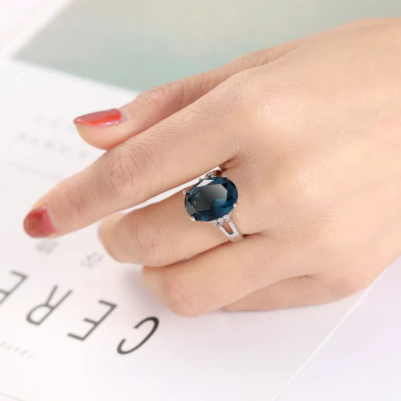Geometric ellipse-shaped copper ring with zircon decoration in blue black finish on a grey background.