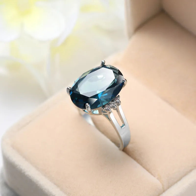 Geometric ellipse-shaped copper ring with zircon decoration in blue black finish on a grey background.