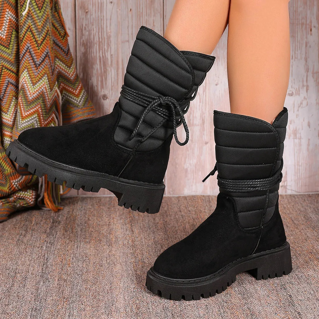 Women's black chunky heel snow boots with suede upper, rubber sole, and lace-up design on wooden floor