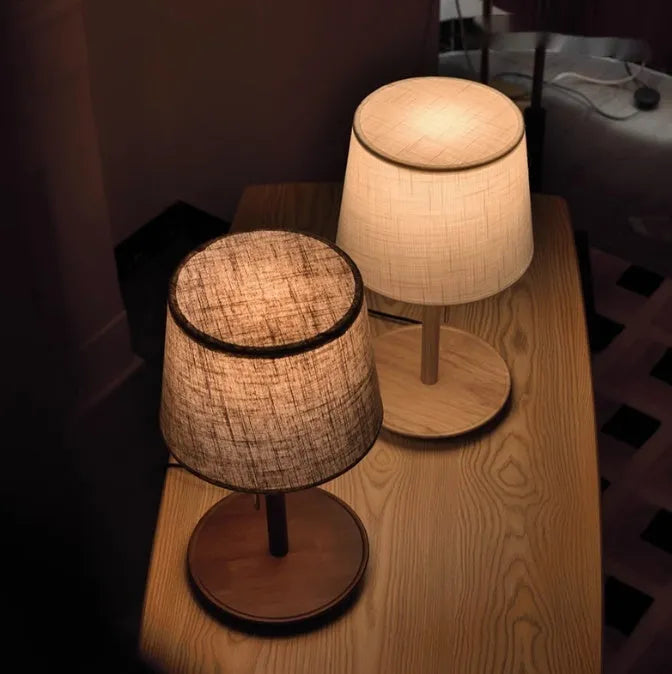 Walnut colour solid wood bedside lamp with a white fabric shade on a wooden surface.