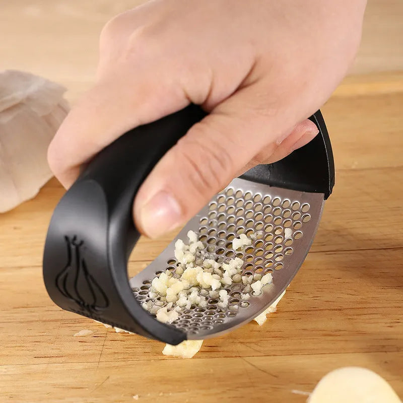 Stainless steel garlic press in green colour with ergonomic handle, measuring 11cm by 7cm on a kitchen counter