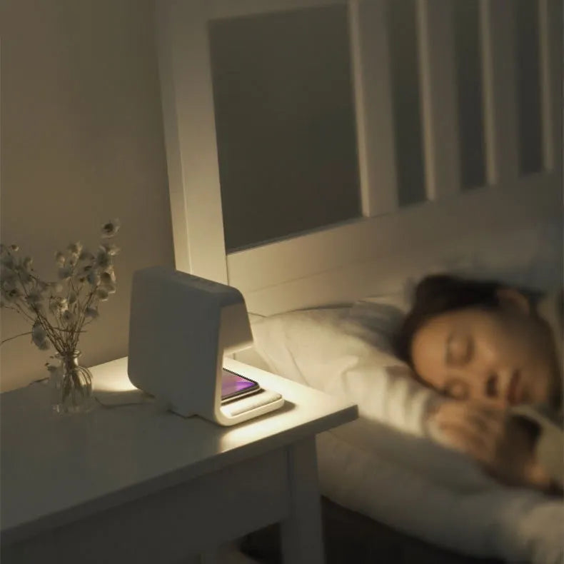 White bedside lamp with integrated wireless charging pad, LCD alarm clock screen, and touch-sensitive dimming controls.