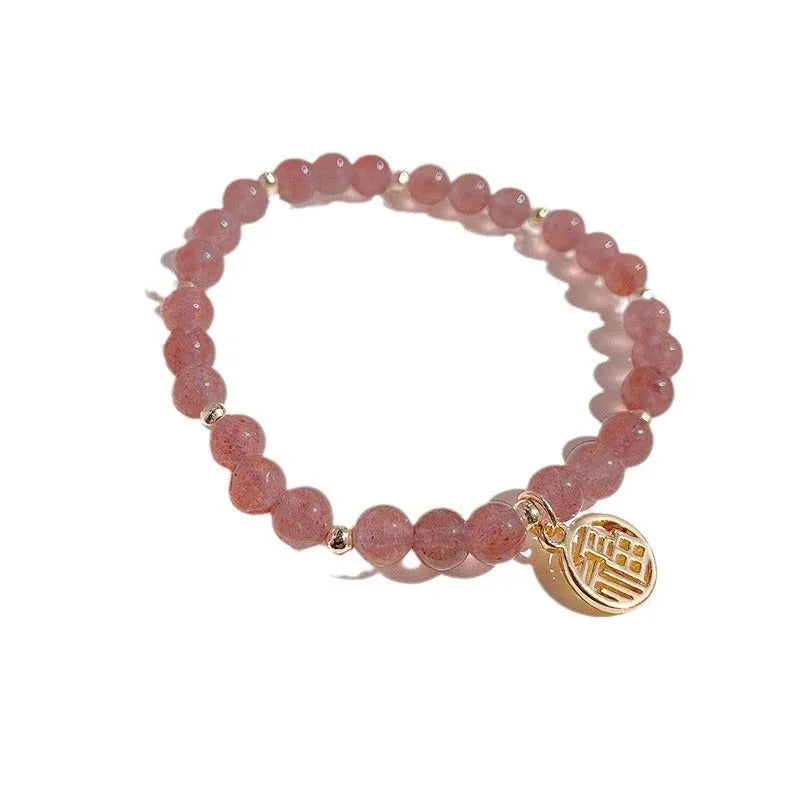 Handmade strawberry quartz style glass bead bracelet with a blessing card charm on a wrist.
