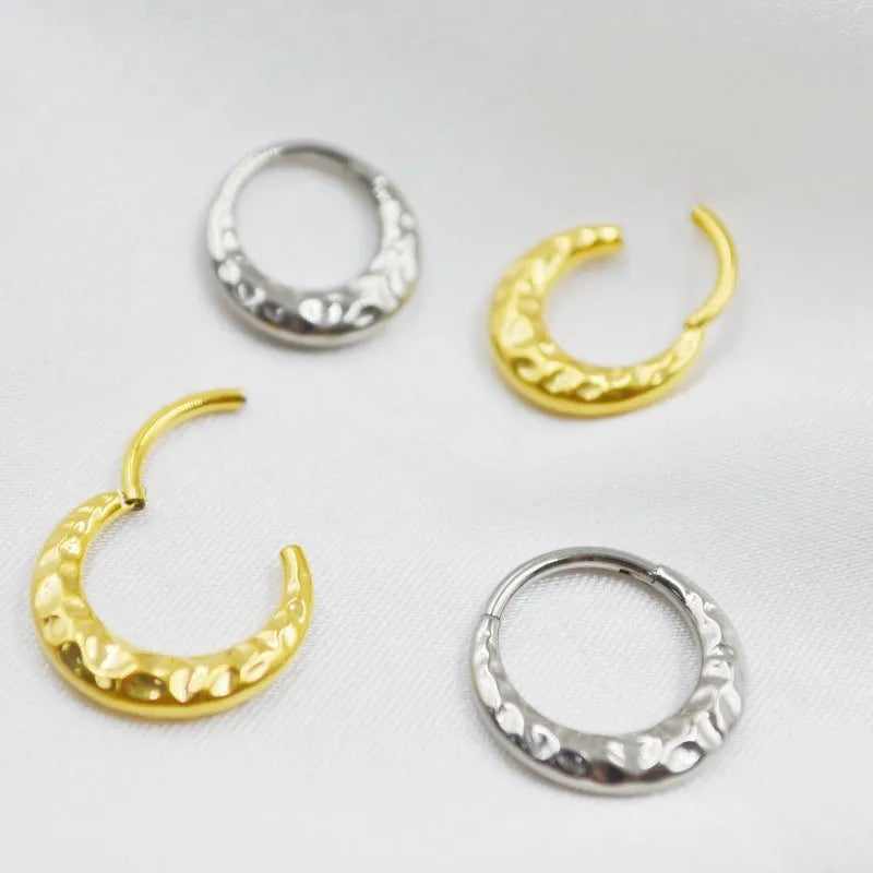Titanium alloy concave-convex carved nose ring in gold and silver colours on a plain background.