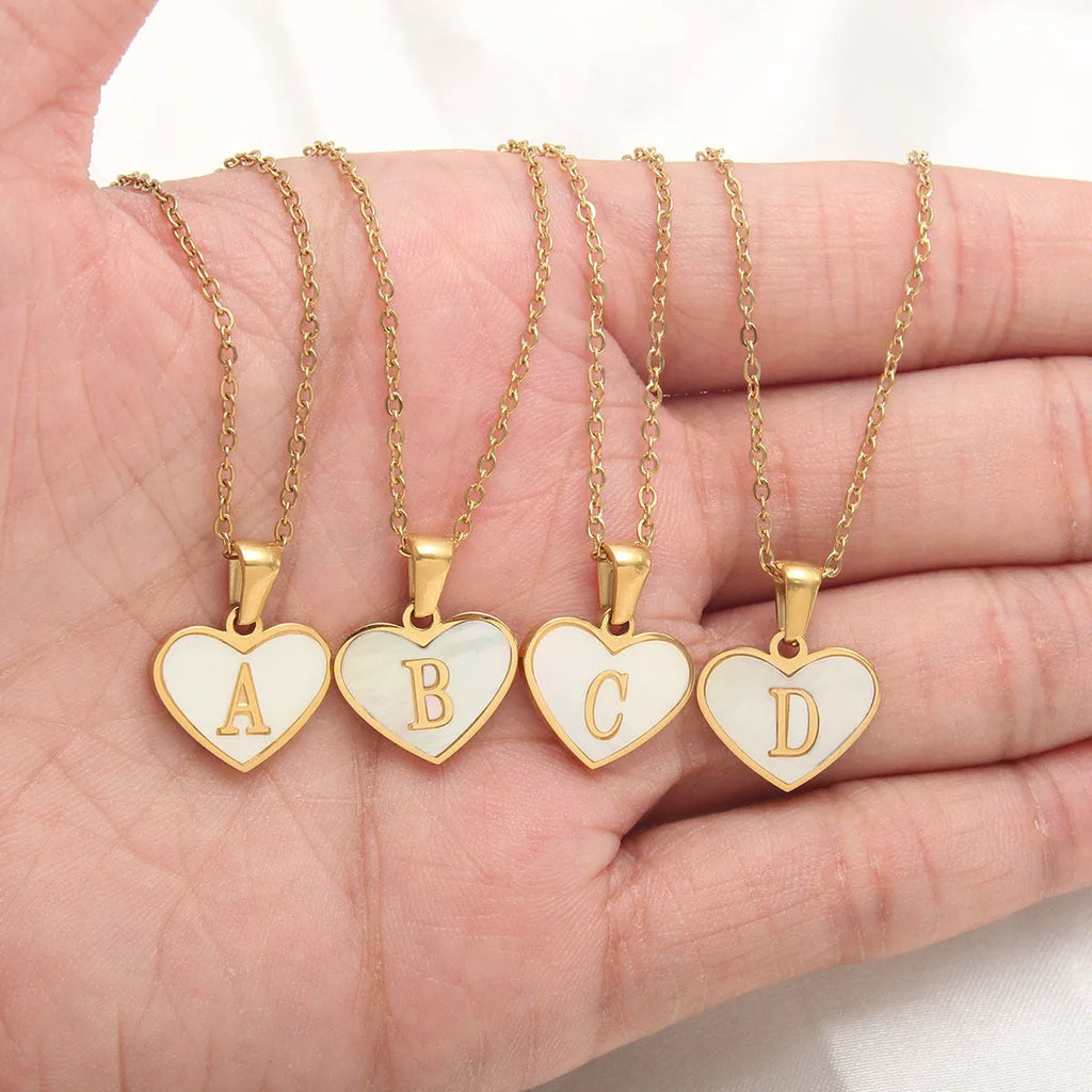 Gold-plated heart-shaped white shell initial necklace on a model, showing the adjustable clavicle chain.