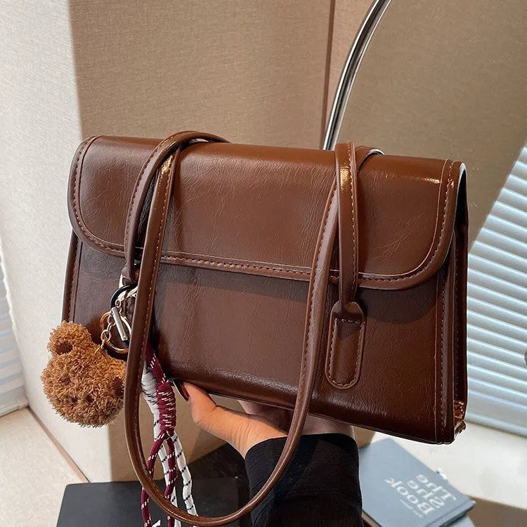 Brown women's structured shoulder bag with horizontal square shape, pendant accessory, and double joint shoulder straps