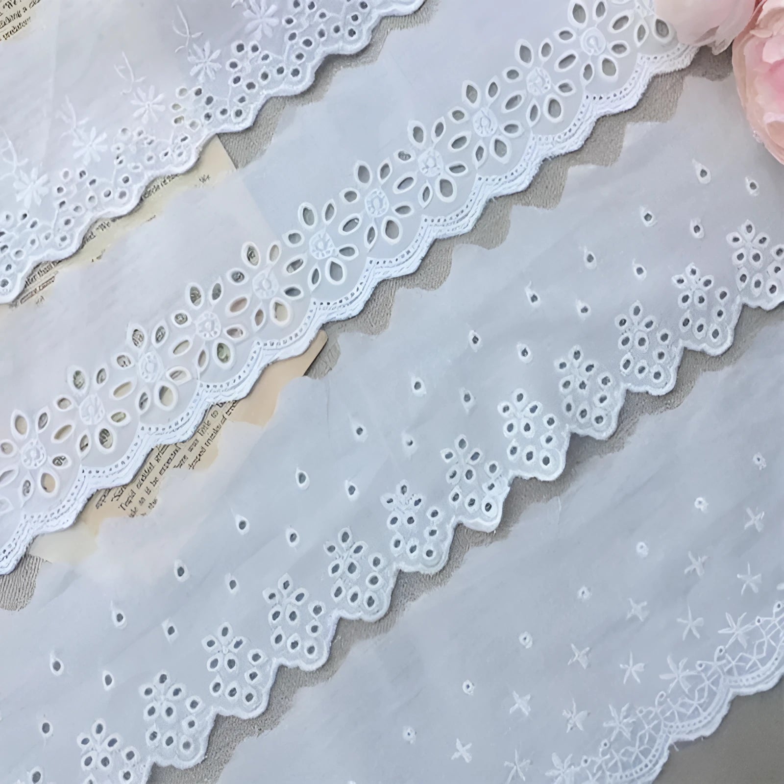 Reel of white embroidered cotton lace trim with a cutout design, showing four different width styles for DIY sewing.