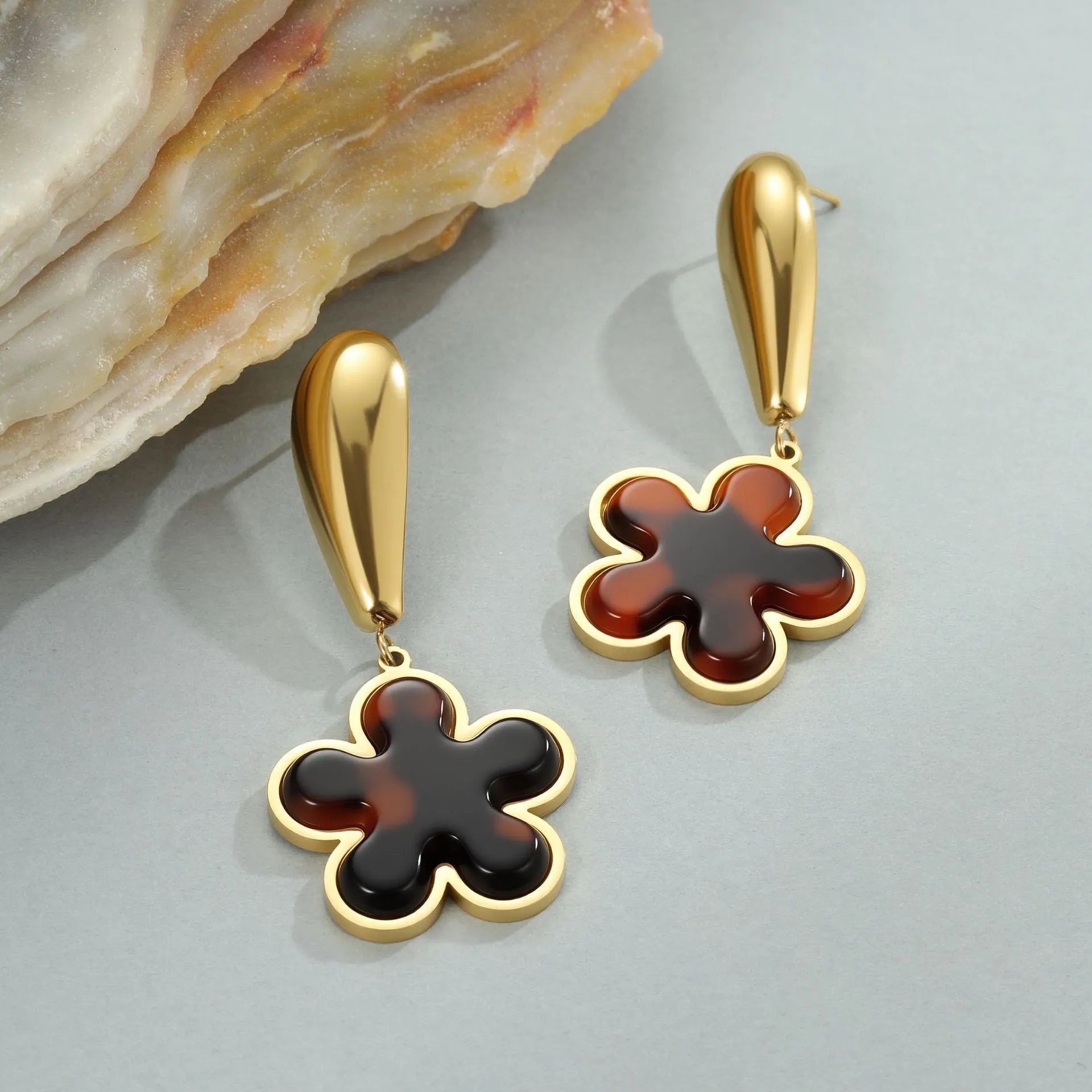 A pair of women's tortoiseshell resin earrings in hawksbill colour, showing heart-shaped and geometric flower designs on stainless steel with 18K plating.