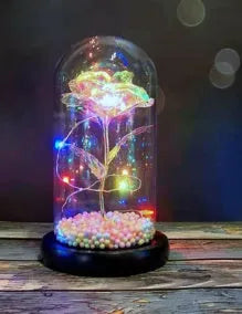 Gold artificial roses inside a clear glass dome ornament with LED lights and decorative accessories.