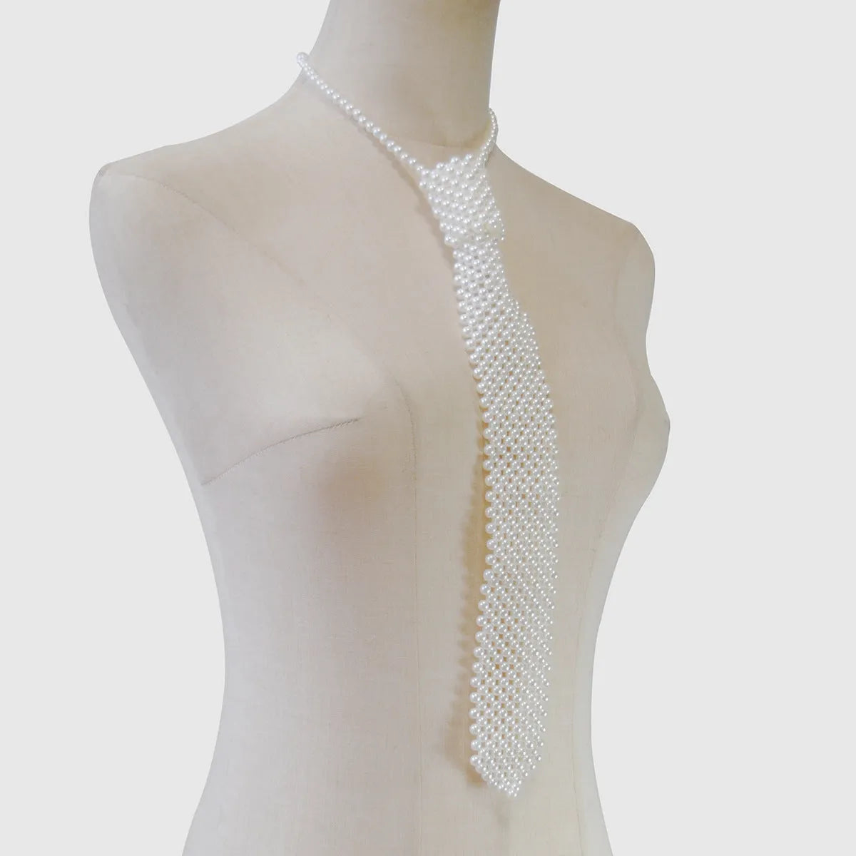 Close-up of a white imitation pearl body chain with an adjustable alloy tie clasp on a dark background.