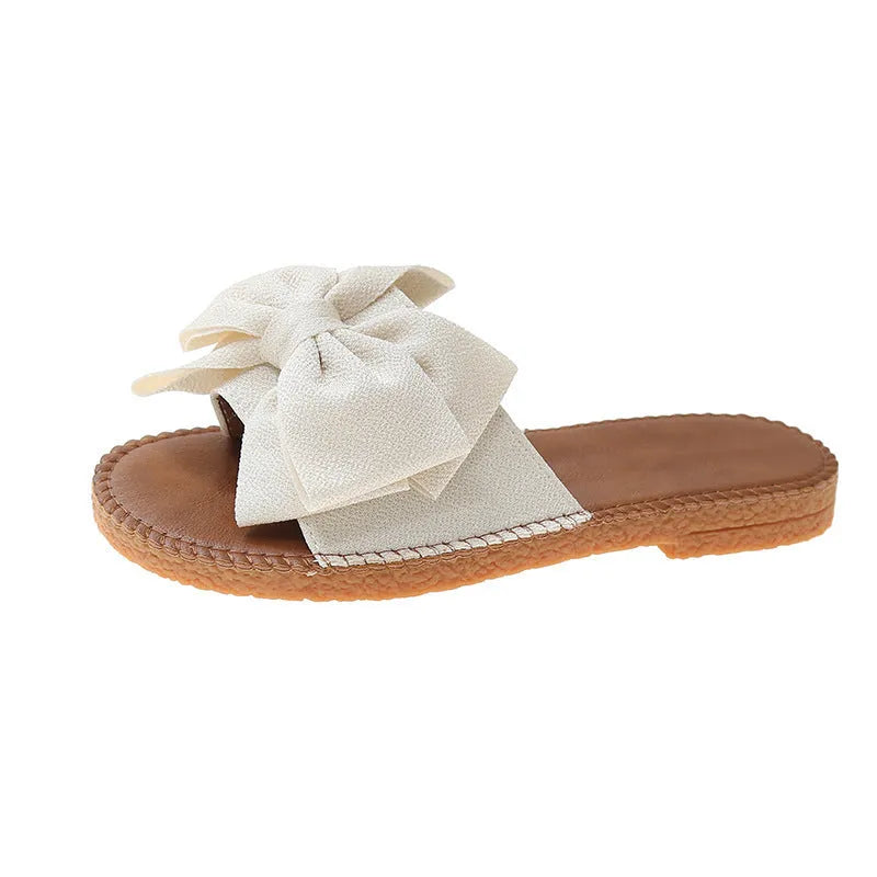 Women's beige suede slip-on sandals with a bow and soft rubber flat sole.