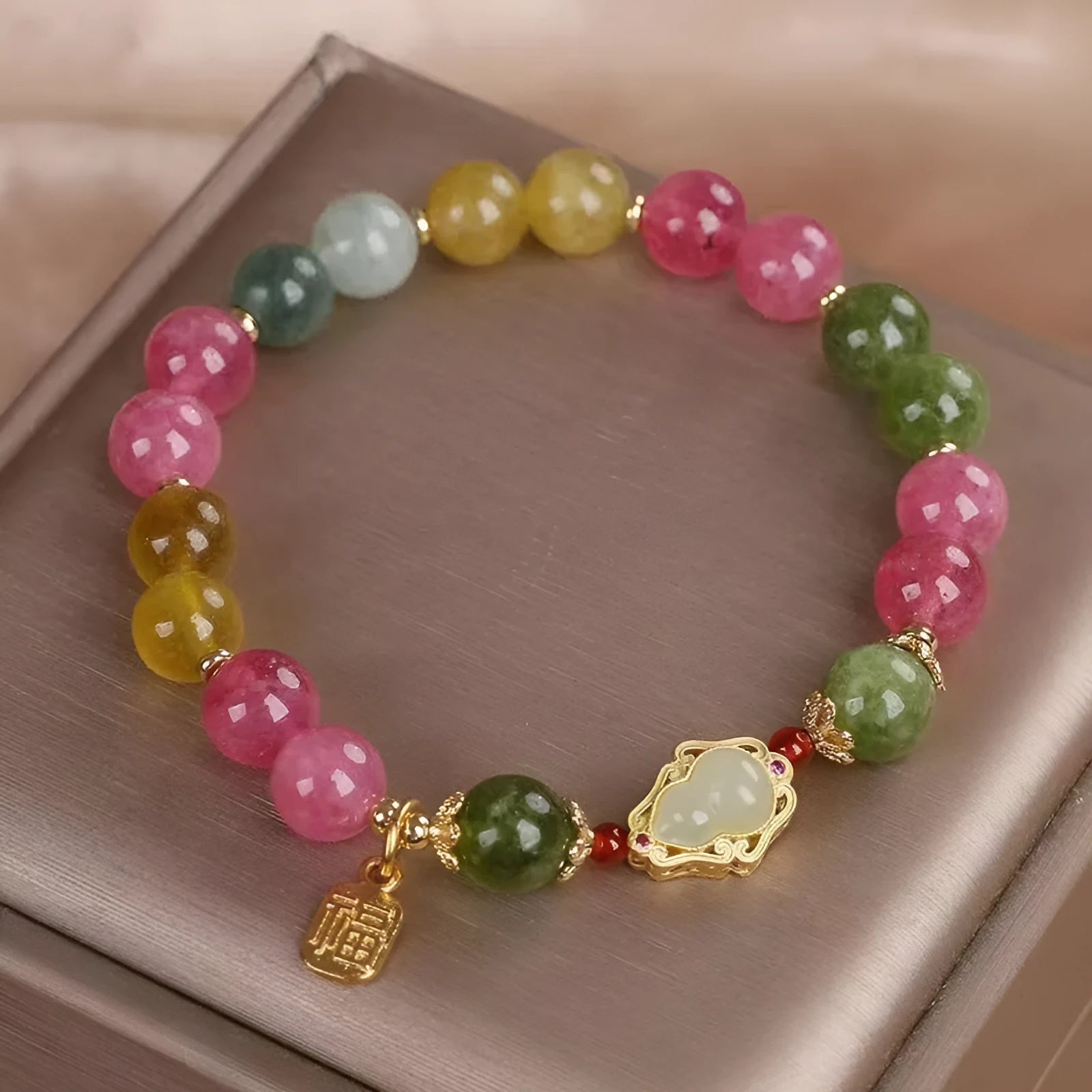 Close-up of a women's bracelet with a colourful tourmaline gourd charm and electroplated floral links.