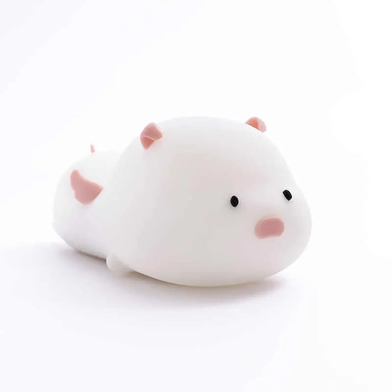 Cute pink silicone pig night light with sleeping design on a bedside table.