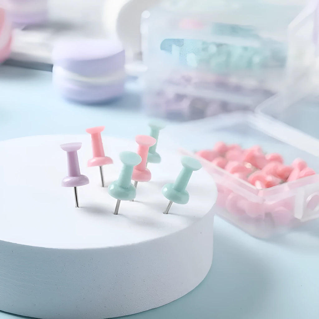 Box of plastic push pins in mint green, pink, and lavender colours, showing large and small thumbtacks for bulletin boards.