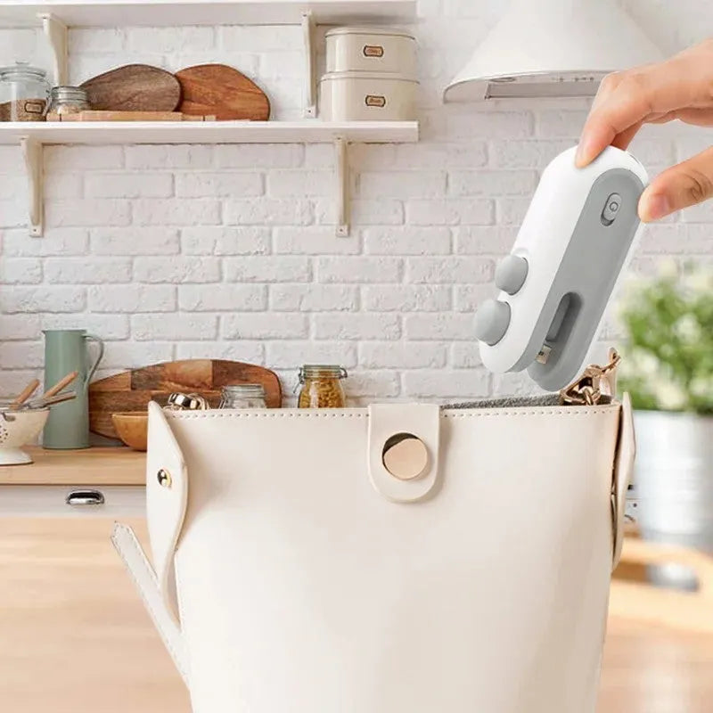 Blue and white handheld USB heat sealer with cutter blade on a magnetic metal surface.