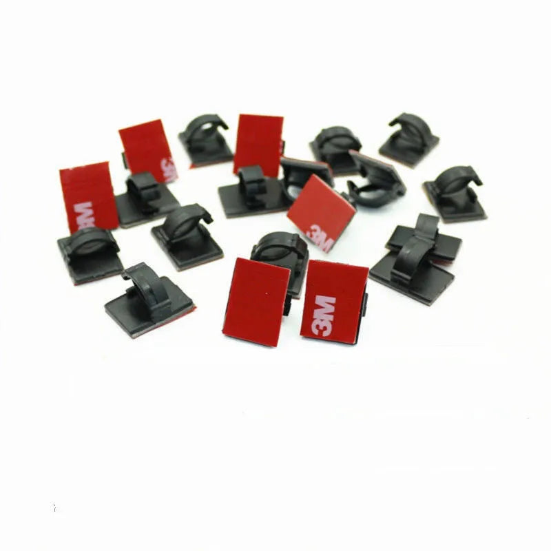 Black and white plastic self-adhesive cable clamps for wire management on a table.