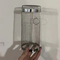 Stainless steel cylindrical rolling grill basket for BBQ with wire mesh, shown with vegetables inside.