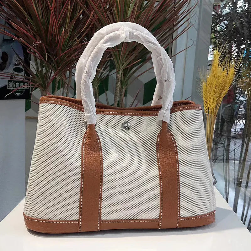 Women's canvas tote bag with leather accents showing internal zipper compartments and soft carry handle