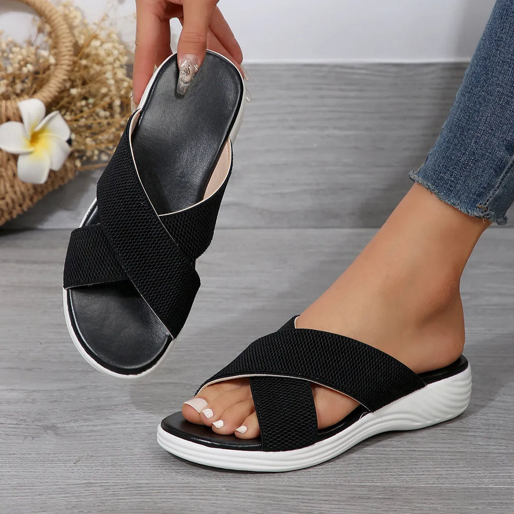 Black women's flat wedge peep-toe slippers with a cross strap and thick rubber sole.