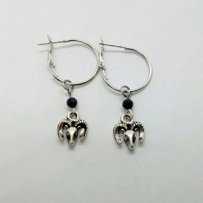 Close-up of a pair of silver round hoop earrings with a detailed Tibetan antelope engraving, shown against a plain background.