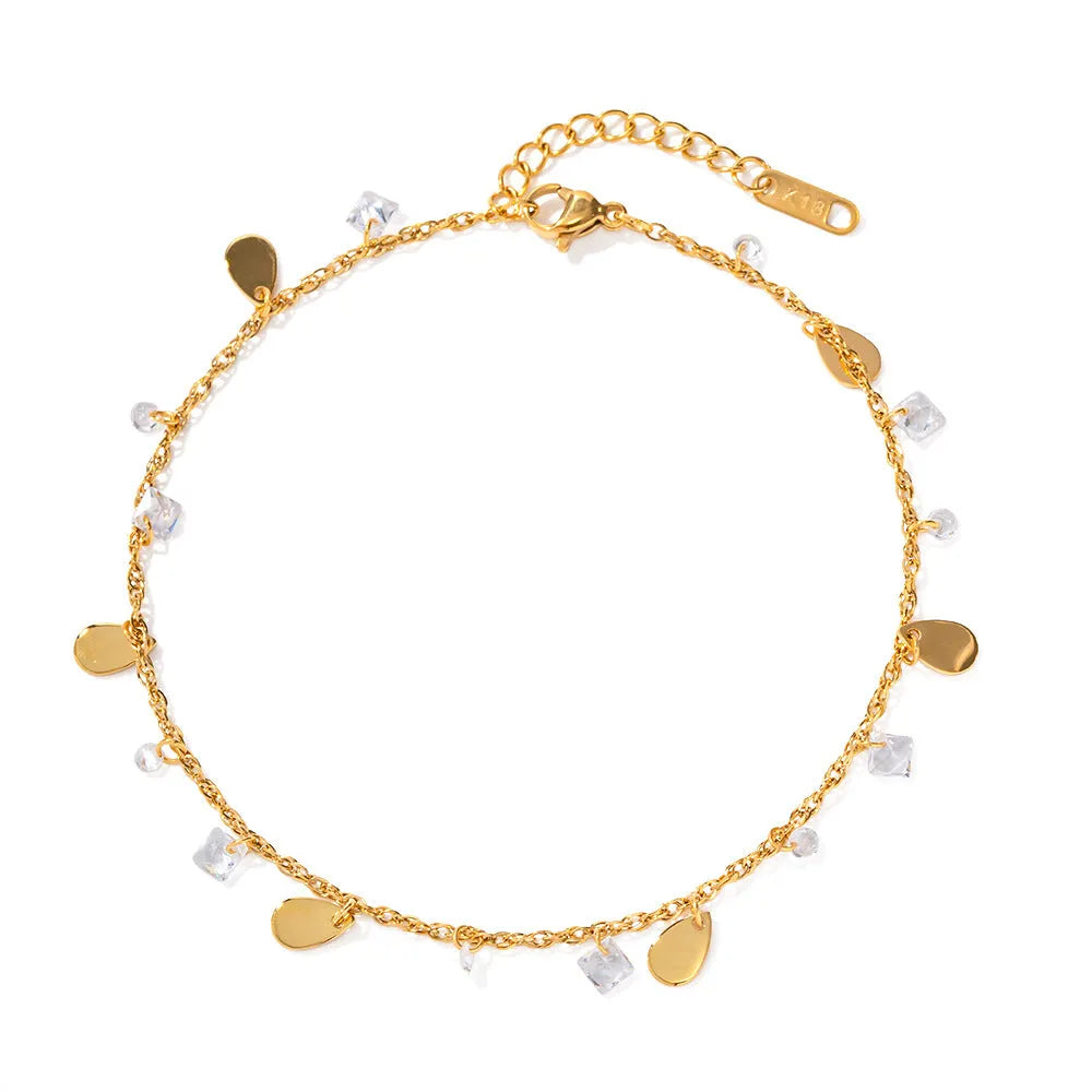 Close-up of a stainless steel anklet with a geometric water drop pendant and dangling tassel charm on an ankle.