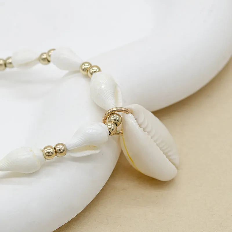 White shell necklace with conch-shaped pendant on adjustable chain, showing mother-of-pearl texture.