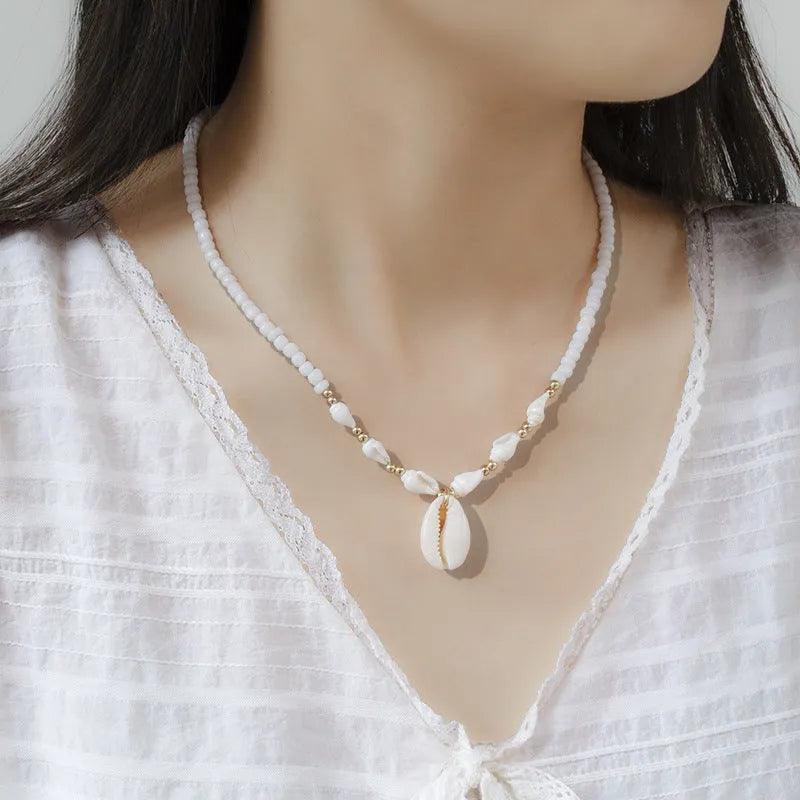 White shell necklace with conch-shaped pendant on adjustable chain, showing mother-of-pearl texture.
