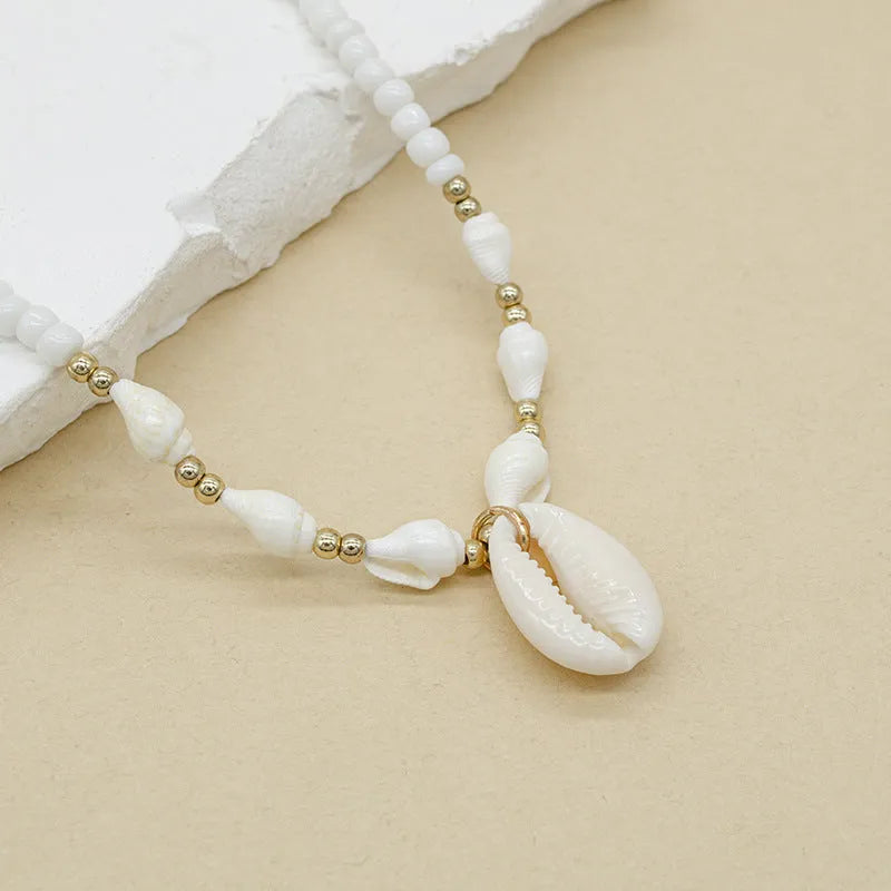 White shell necklace with conch-shaped pendant on adjustable chain, showing mother-of-pearl texture.