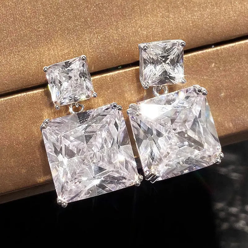 A pair of geometric square design earrings in a gold metallic finish on a white background.