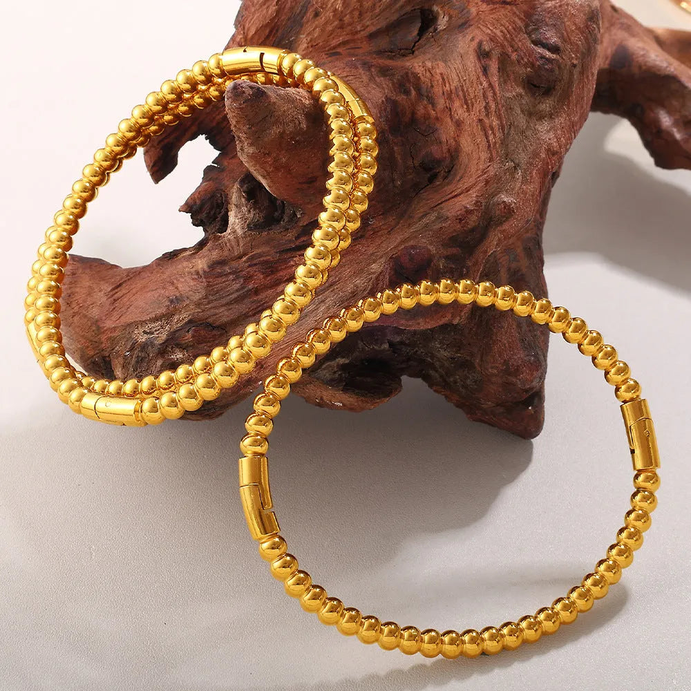 Stainless steel open-end bracelet with a buckle closure and circle design, shown in an electroplated gold colour.