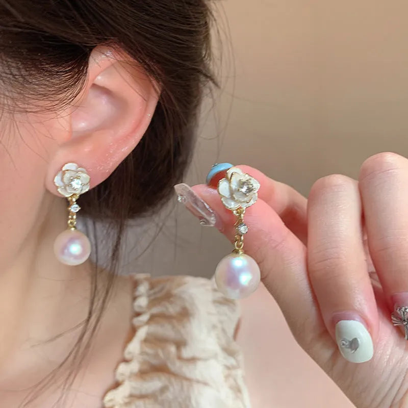Close-up of camellia flower-shaped stud earrings for women in a pearl-like finish.