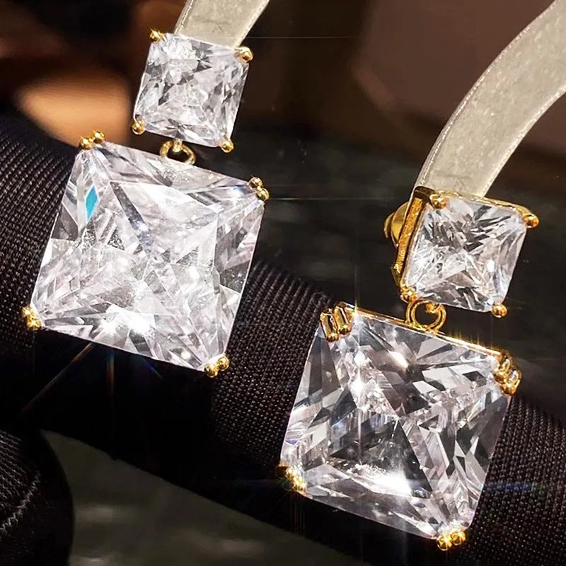 A pair of geometric square design earrings in a gold metallic finish on a white background.