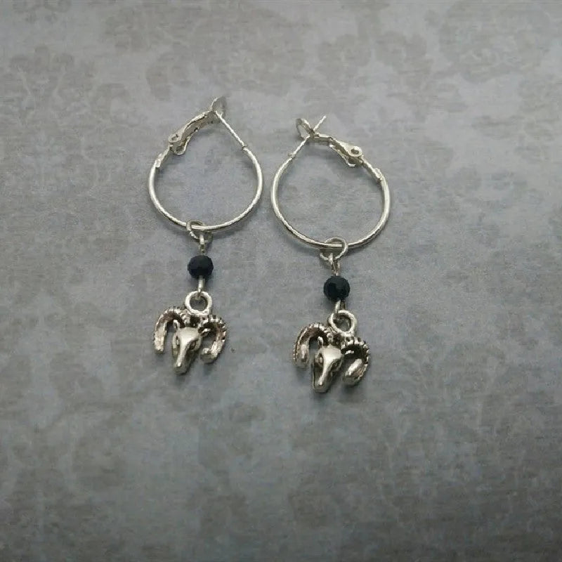 Close-up of a pair of silver round hoop earrings with a detailed Tibetan antelope engraving, shown against a plain background.