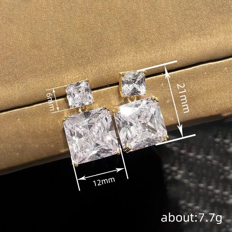 A pair of geometric square design earrings in a gold metallic finish on a white background.