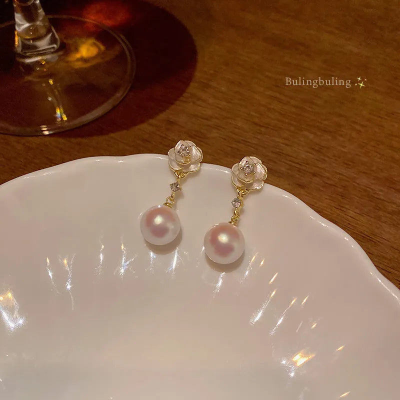 Close-up of camellia flower-shaped stud earrings for women in a pearl-like finish.