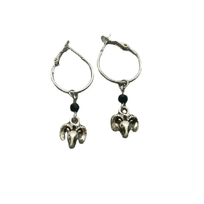 Close-up of a pair of silver round hoop earrings with a detailed Tibetan antelope engraving, shown against a plain background.