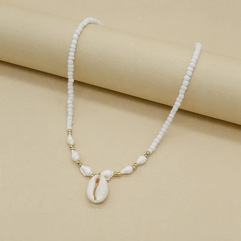 White shell necklace with conch-shaped pendant on adjustable chain, showing mother-of-pearl texture.