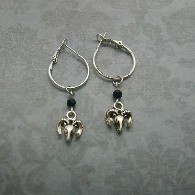 Close-up of a pair of silver round hoop earrings with a detailed Tibetan antelope engraving, shown against a plain background.